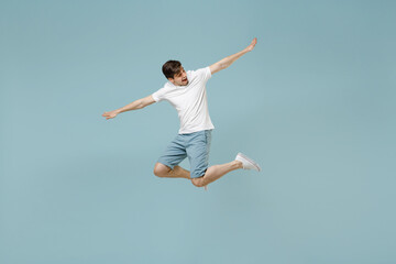 Fototapeta na wymiar Full length young fun happy european man 20s wearing white casual basic t-shirt jump high with outstretched hands isolated on pastel blue color background studio portrait. People lifestyle concept