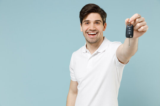 Young happy smiling fun caucasian man 20s in white casual basic t-shirt hold in hand giving cark key fob keyless system isolated on pastel blue background studio portrait. People lifestyle concept