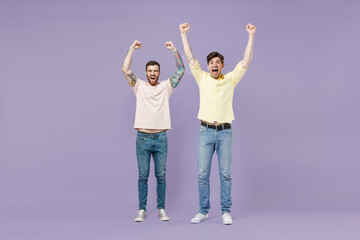 Obraz premium Full length overjoyed excited two young happy men friends together walk in casual t-shirt walk do winner gesture clench fist isolated on purple background studio People friendship lifestyle concept