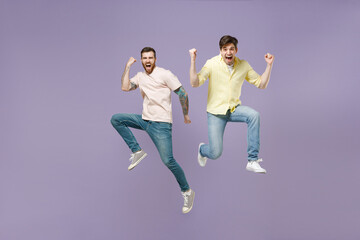 Fototapeta na wymiar Full length two young overjoyed cool men friends together in casual tshirt do winner gesture clench fist jump high celebrating scream yes isolated on purple background studio People lifestyle concept