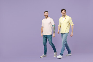 Fototapeta premium Full length side view two young happy men 20s friends together in casual t-shirt walking going strolling lokk camera isolated on purple background studio portrait People friendship lifestyle concept