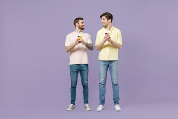 Full length fun happy two young men friends together in casual t-shirt use mobile cell phone chat...
