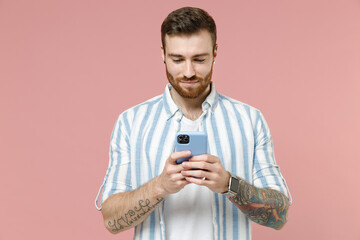 Young smiling happy caucasian unshaven man 20s in blue striped shirt holding mobile cell phone chat...