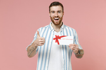 Young surprised overjoyed caucasian unshaven man in blue striped shirt hold gift voucher flyer mock...