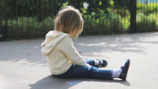 Adorable toddler girl drawing with colorful chalks on asphalt