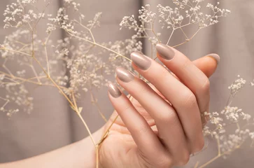 Wall murals Manicure Female hand with glitter beige nail design. Female hand hold autumn flower. Woman hand on beige fabric background