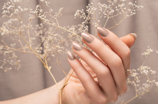 Female hand with glitter beige nail design. Female hand hold autumn flower. Woman hand on beige fabric background