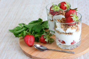 strawberry dessert with yogurt, granola and mint leaves on the cutting board background with a teaspoon and tablecloth