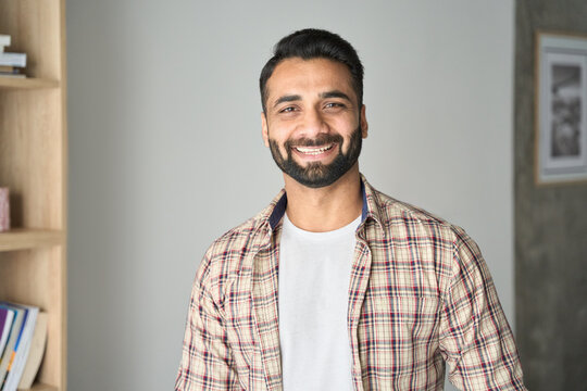 Headshot portrait of attractive confident indian Hispanic man with toothy smile looking at camera at modern living room. Latin businessman posing in casual stylish look at home office.