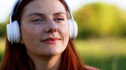Close up portrait of beautiful girl listening music with headphones on sunny day while walking in city park