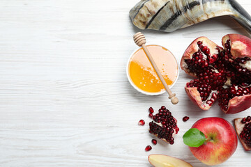 Honey, pomegranate, apples and shofar on white wooden table, flat lay with space for text. Rosh...