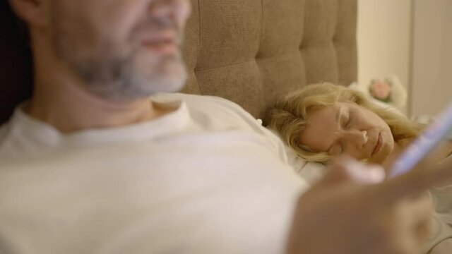 Lustful man in his 40s scrolling photos on dating app, his wife asleep, betrayal