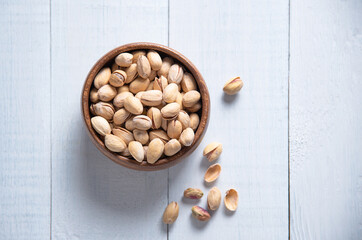 Pistachio nuts in a brown bowl on a white wooden background. Top view and copy space