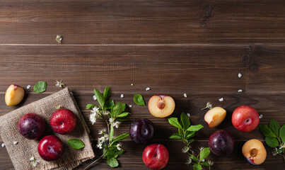 concept flat lay a few juicy red plums with branch blossom flowers  on a brown wood background. Top...
