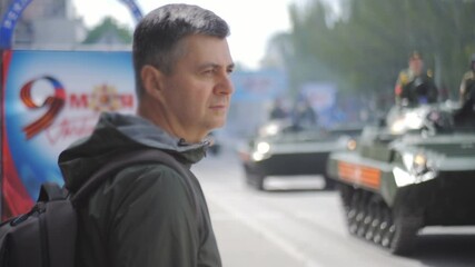 A man watches military vehicles moving through the city during a military parade