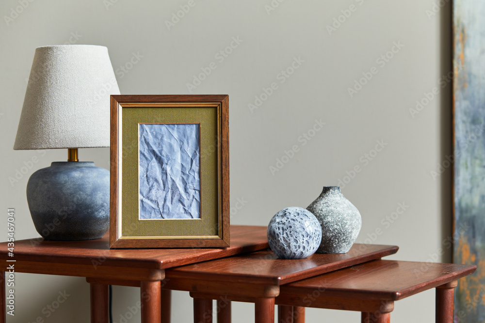 Wall mural Elegant composition on the wooden stools with mock up picture frame, table lamp, vase and personal accessories in modern home decor. Template.