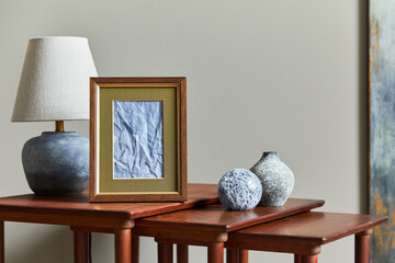 Elegant composition on the wooden stools with mock up picture frame, table lamp, vase and personal...