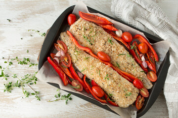 halibut fillet in bread crumbs with vegetables on a baking sheet