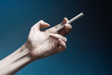 World No Tabacco day. A pale, crooked female hand, close-up, holding a new cigarette. Dark blue background. The concept of nicotine addiction