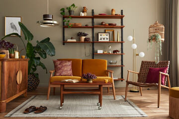 Stylish interior of living room with honey yellow sofa, wooden bookcase, plants, commode, picture...