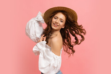 Laughing  red-haired white woman having fun  in studio on pink background. Perfect wavy hairs, straw har, white summer top with sleeves.