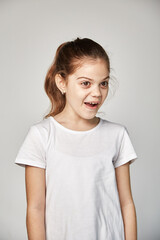 Fototapeta premium A cute 10-year-old model with an oriental appearance expresses surprise, dressed in a white T-shirt. Portrait of a studio shot on a white copy space. Expression of emotions