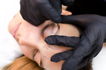 the permanent makeup artist stretches the skin in the area of the eyebrows to perform the tattoo - obrazy, fototapety, plakaty