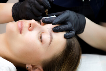 the permanent makeup artist performs a tattoo of the eyebrows according to the markings drawn...