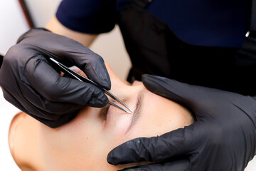 the permanent makeup master performs plucking of unnecessary hairs in the eyebrow area after the...