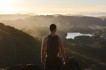 An inspiring and motivational photo of a young male hiker ascending a peak and looking at the view triumphantly during a golden sunset.