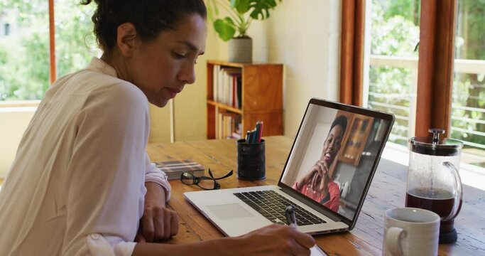 African american woman taking notes while having a video call on laptop at home