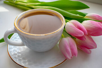 Obraz na płótnie Canvas A cup of hot coffee with a bouquet of pink tulips on a white table background.