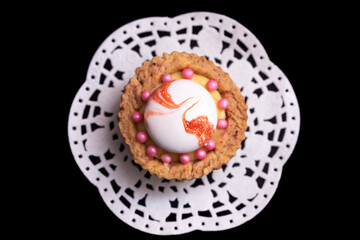 Brown cupcake with white meringue, lemon cream and pink candies, on white paper