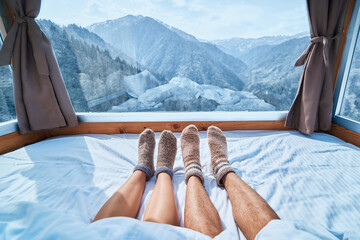 Lover couple in knitted warm socks lying on a soft cozy bedroom with snowy mountains view in a...