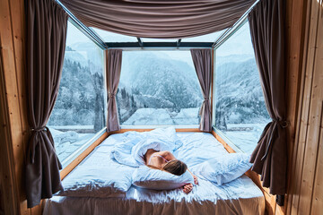 Tranquil serene calm woman sleeping on a soft white cozy comfortable warm bed in room with snowy...