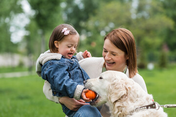 cheerful autistic kid giving ball to dog near mother in park