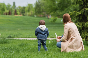 back view of autistic child standing on grass near mother in park