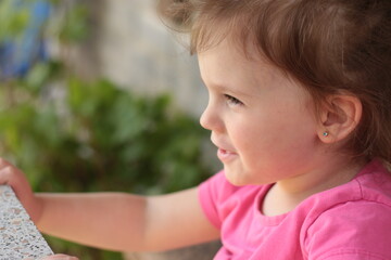 Beautiful little smiling red-haired girl in a pink t-shirt sits at a table outdoors