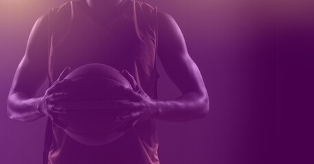 Composition of fit male basketball player holding ball with copy space on purple background