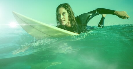 Composition of caucasian female surfer lying on surfboard in sea with copy space on green background © vectorfusionart