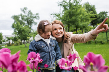 happy mother pointing away near disabled daughter sticking out tongue