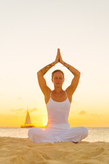 Fototapeta na wymiar Woman meditating, doing yoga, at the beach, sitting by the seashore, dressed in a white outfit at sunset