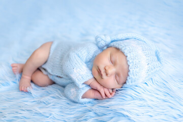 newborn baby sleeps sweetly on a blue background with his hands folded under his cheek, healthy baby sleep