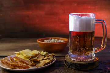 A mug with beer and pistachios with chips on a wooden table.