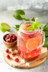 Soft drinks, healthy beverage. Refreshing summer glasses drink raspberry with mint lime and ice on a stone table.