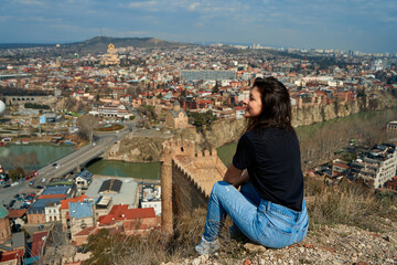 A cute brunette girl enjoys the stunning scenery of Tbilisi from the hill. The whole city at her feet