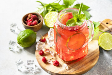 Soft drinks, healthy beverage. Refreshing summer glasses drink raspberry with mint lime and ice on a stone table.