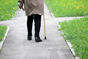 Woman walking with a cane on a street, female legs on sidewalk. Concept of disability, limping person, diseases of the spine, elderly people - obrazy, fototapety, plakaty
