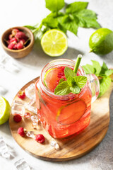 Soft drinks, healthy beverage. Refreshing summer glasses drink raspberry with mint lime and ice on a stone table.