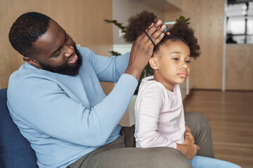 African american father brushing making hairstyle for his young daughter - Powered by Adobe